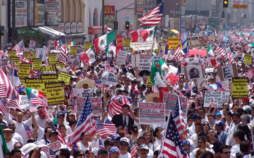 a large number of people fill a city block with pro-immigrant signs and flags
